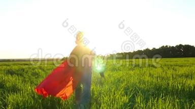 一个穿着超级英雄服装的快乐孩子穿着红色雨衣，在日落的背景下沿着绿色的草坪奔跑。